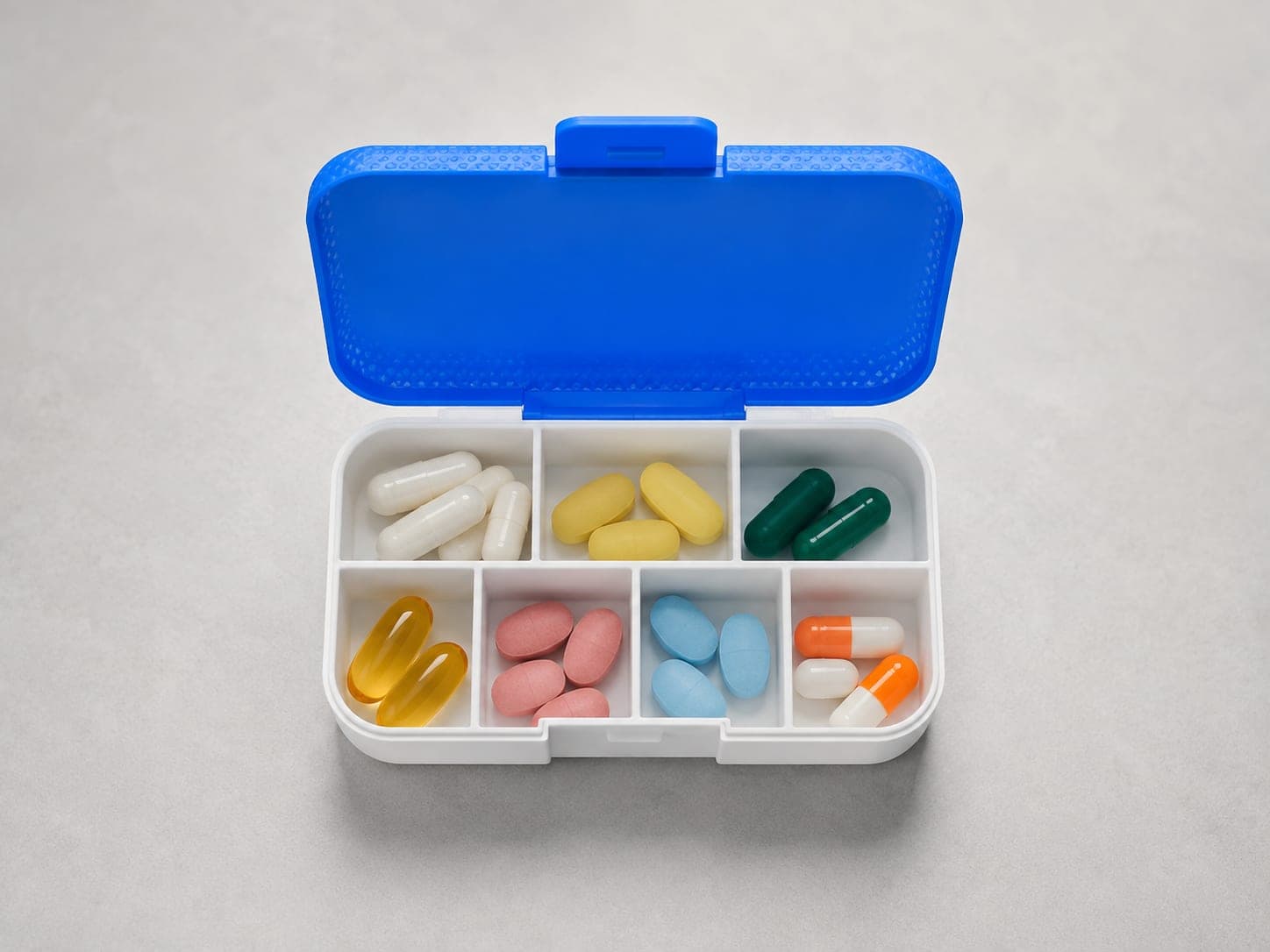 Geöffnete Pillenbox mit sieben Kammern, in denen Kapseln und Tabletten portioniert liegen